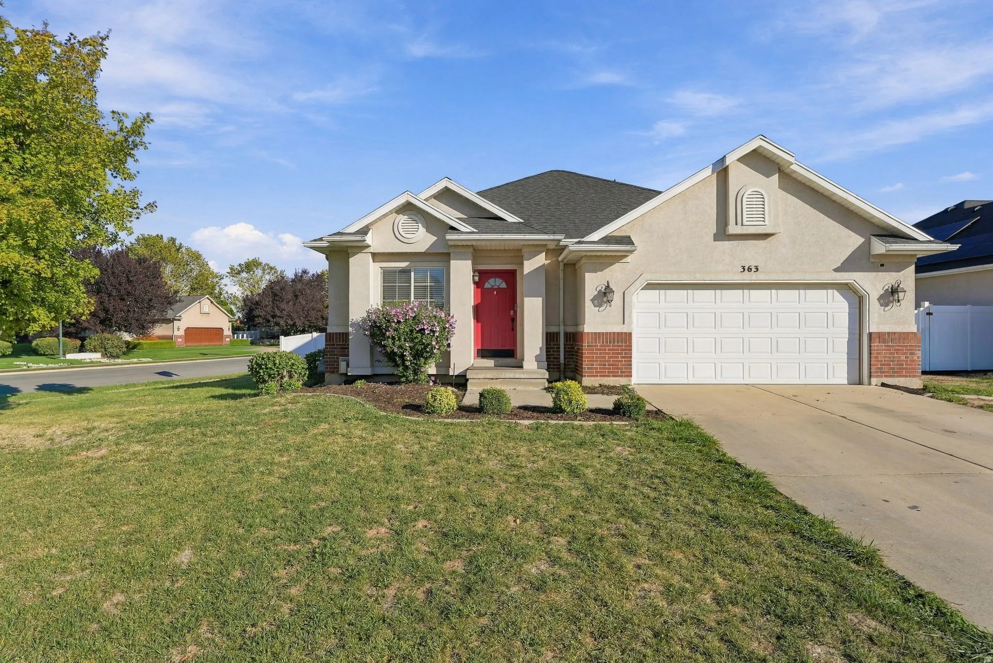 Stucco and brick exterior with a prominent garage, concrete driveway, and established landscaping