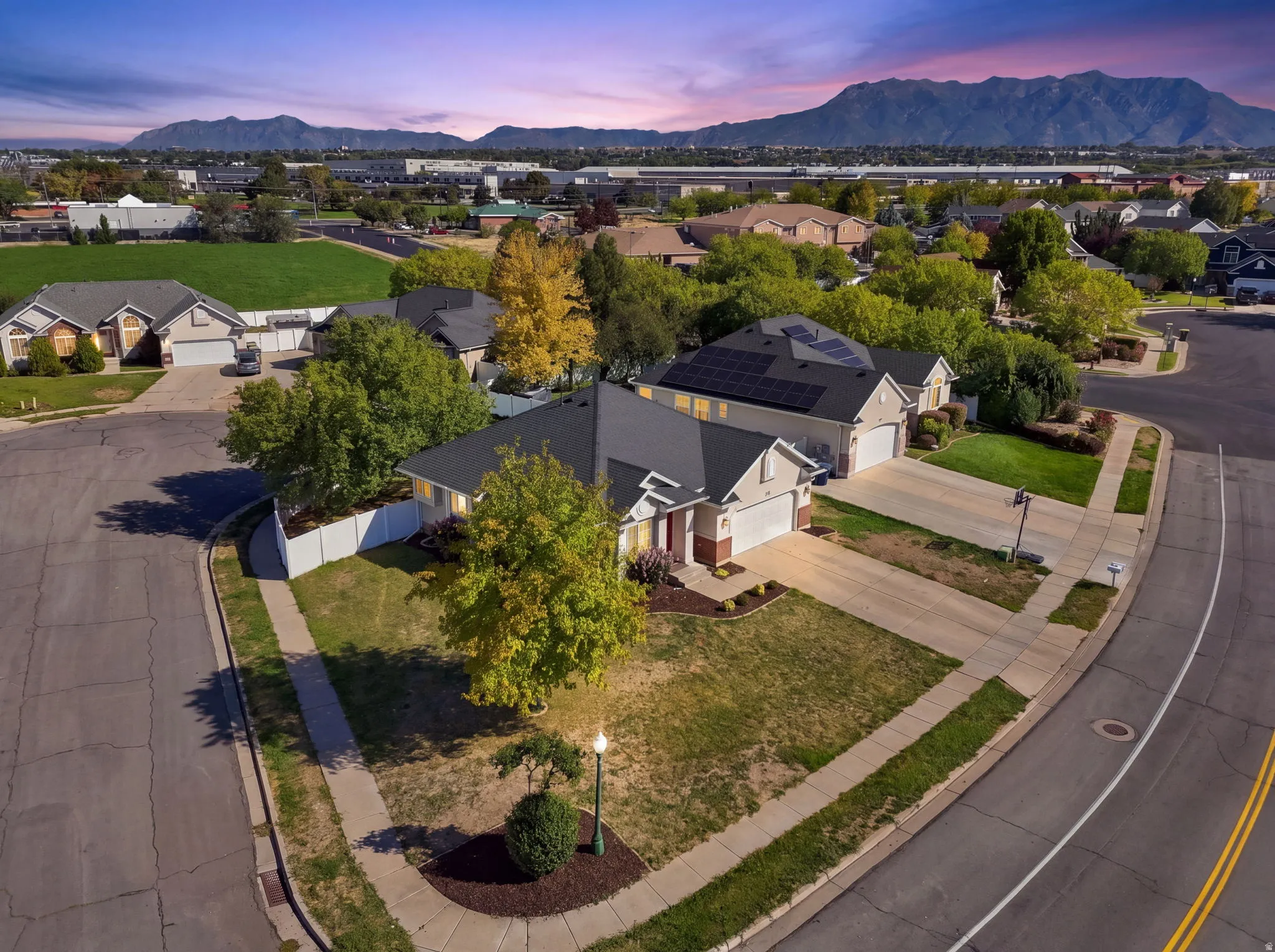 Corner lot property featuring a light-colored exterior, two-car garage, solar panels, mature trees, and mountain scenery