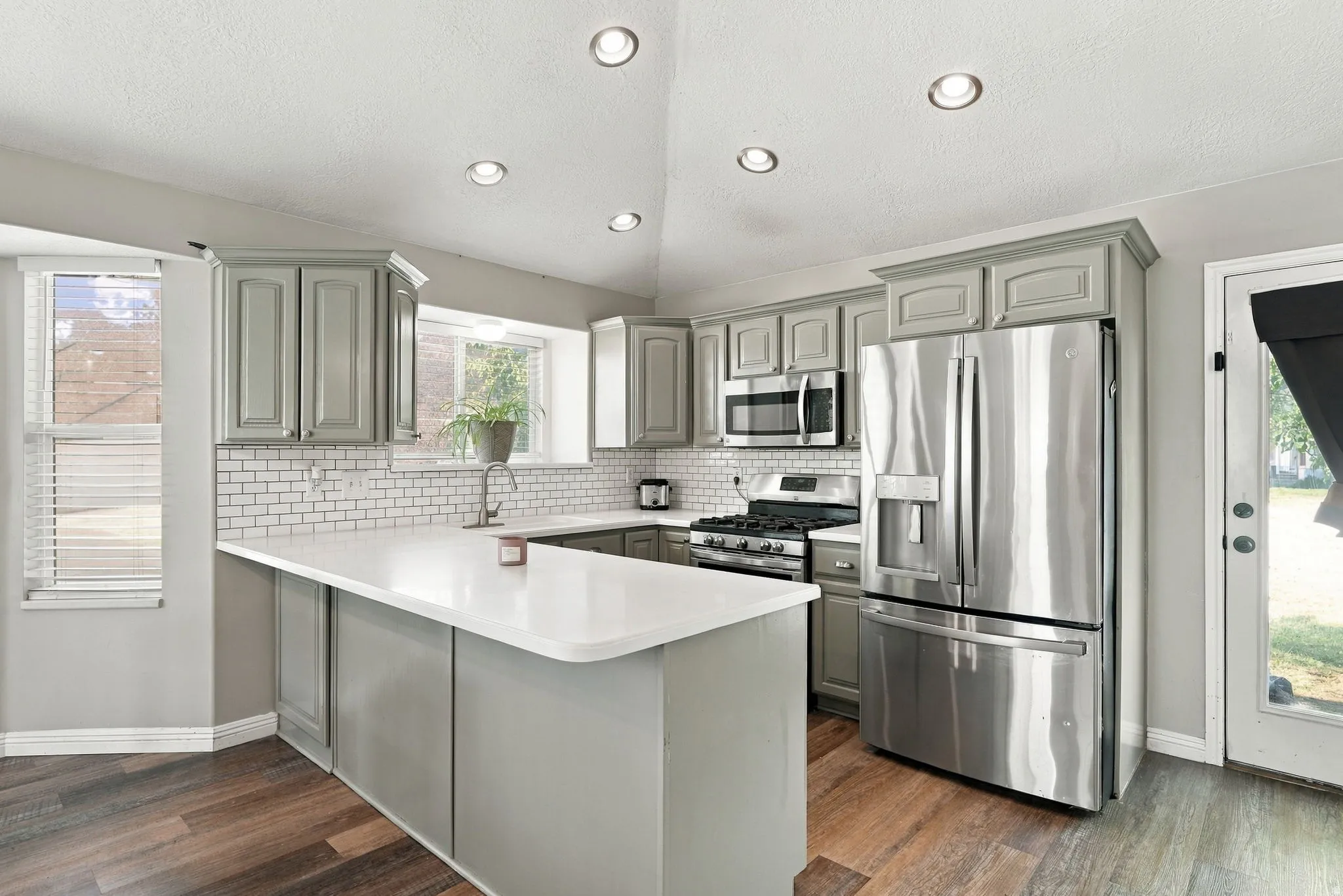 Kitchen featuring wood-finish flooring, recessed lighting, white subway tile backsplash, stainless steel appliances, and an island with a white countertop