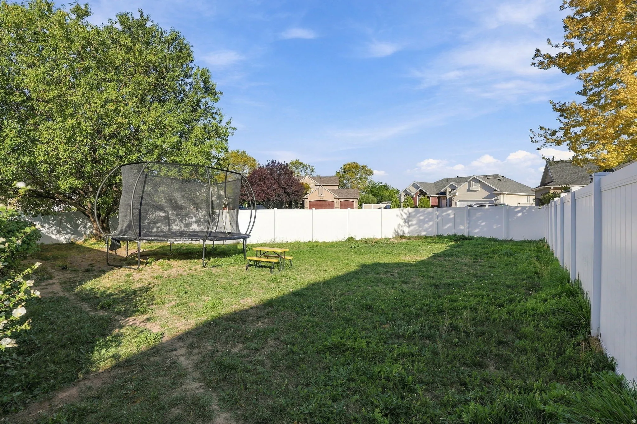 Expansive backyard with a white privacy fence and established trees
