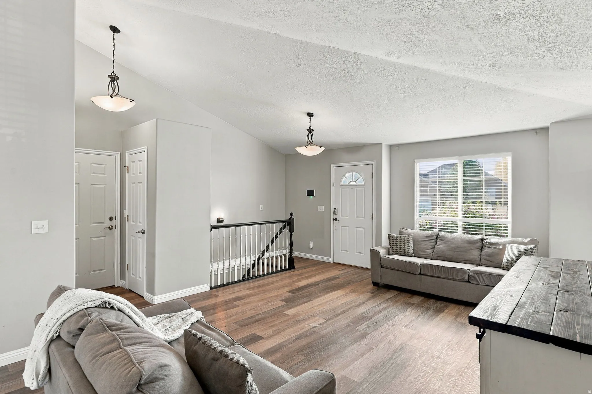 Vaulted ceiling, wood-finish flooring, white paneled doors, staircase with black railing, and a window with blinds