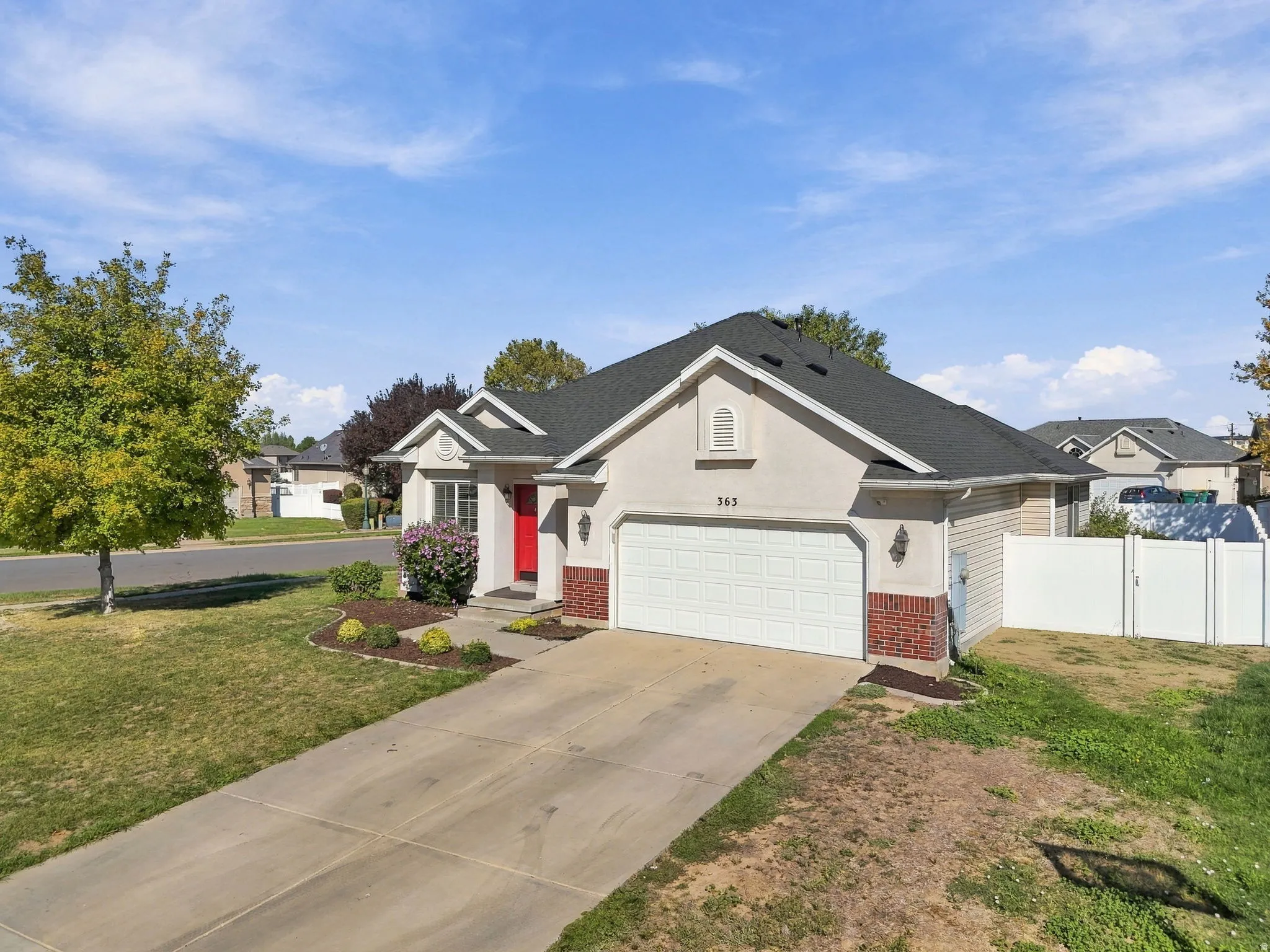 Stucco exterior with brick accent, a prominent red entry door, attached garage, and a white privacy fence