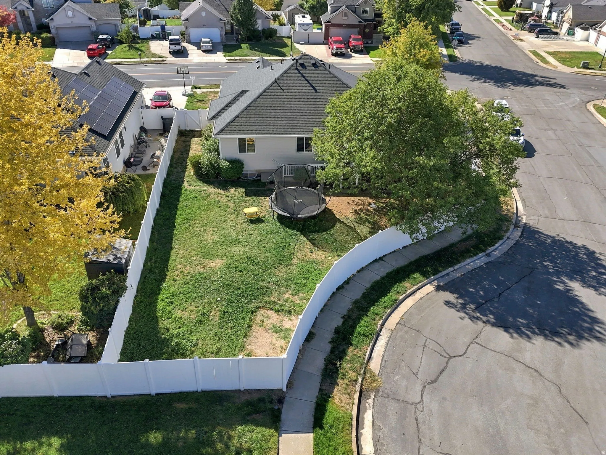 Expansive backyard with a manicured lawn, established trees, and white privacy fencing