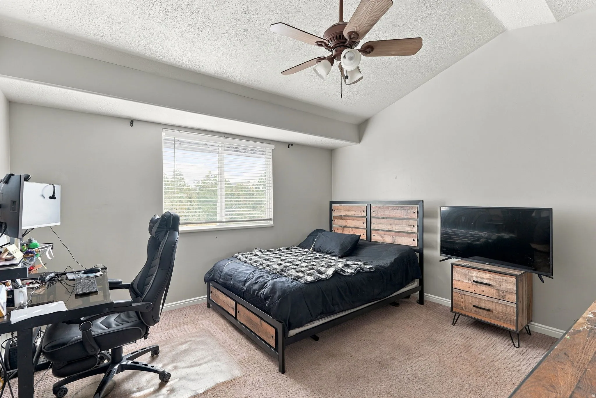 Vaulted ceiling featuring a ceiling fan with integrated lighting, window with blinds, and neutral tone carpeting
