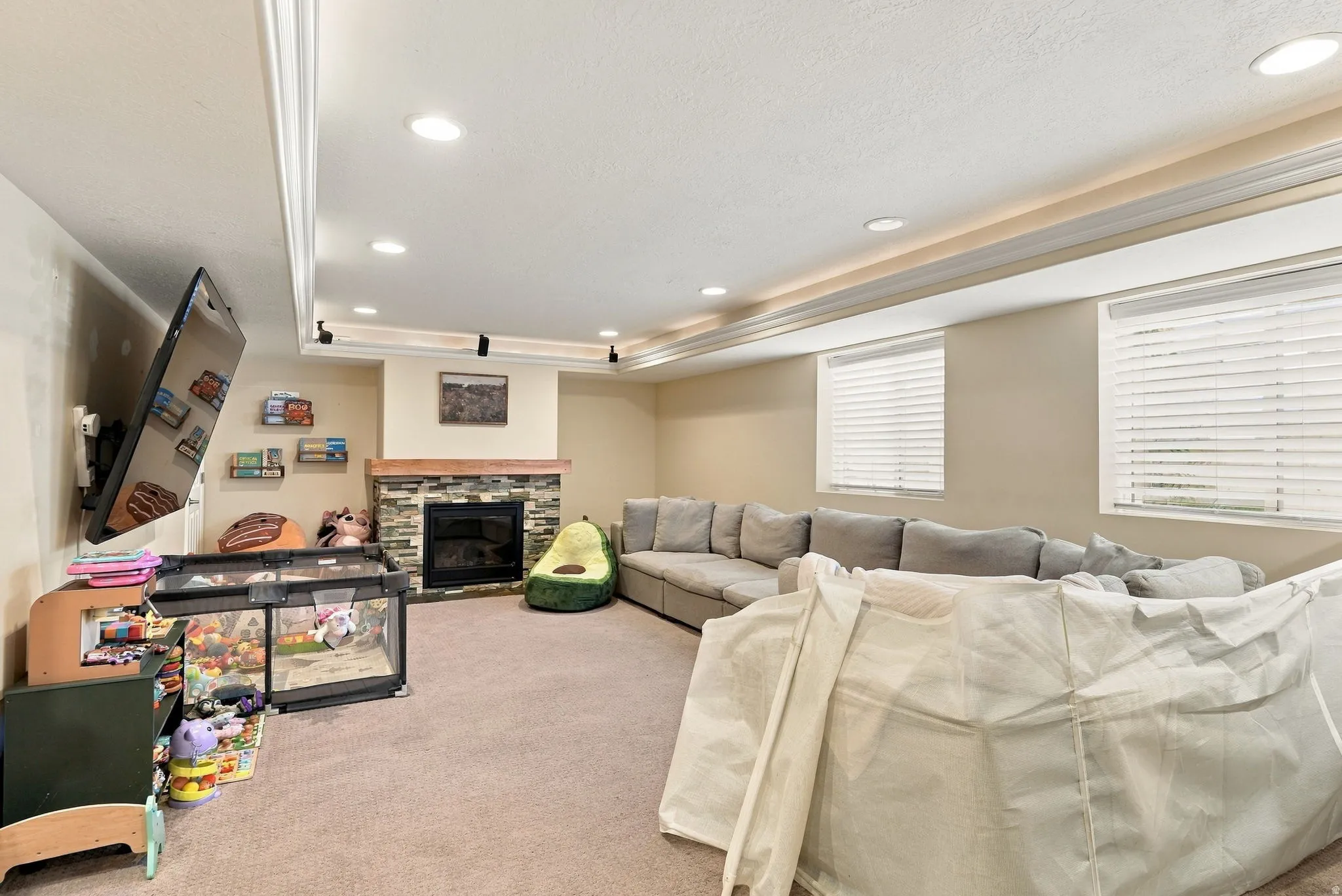 Carpeted lower level with a stone-surround fireplace, wood mantel, recessed lighting, and crown molding