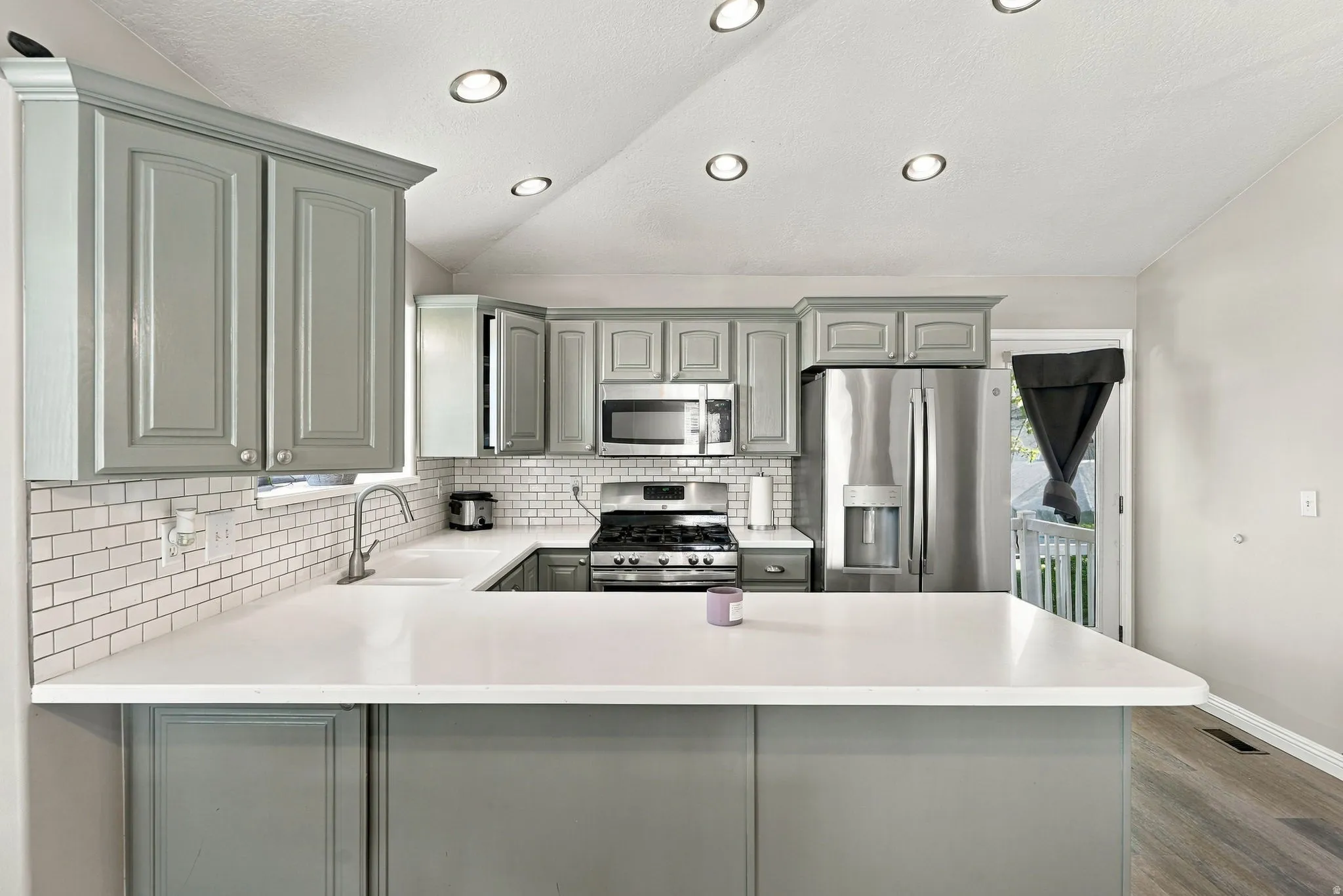 Kitchen featuring light gray cabinetry, white countertops, subway tile backsplash, stainless steel appliances, and recessed ceiling lighting