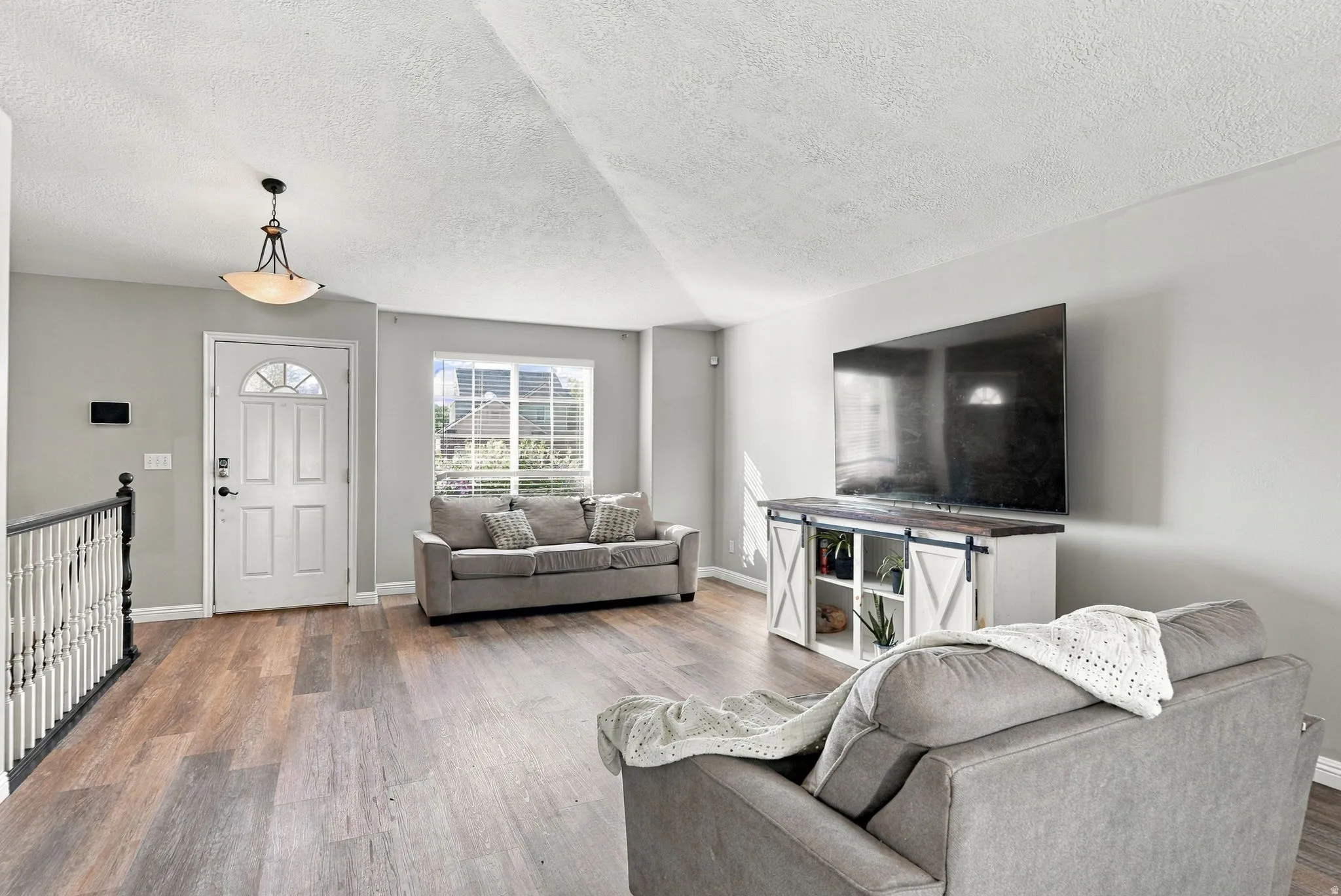 Spacious living area featuring wood-finish flooring, abundant natural light, and a white paneled entry door with an arched glass insert