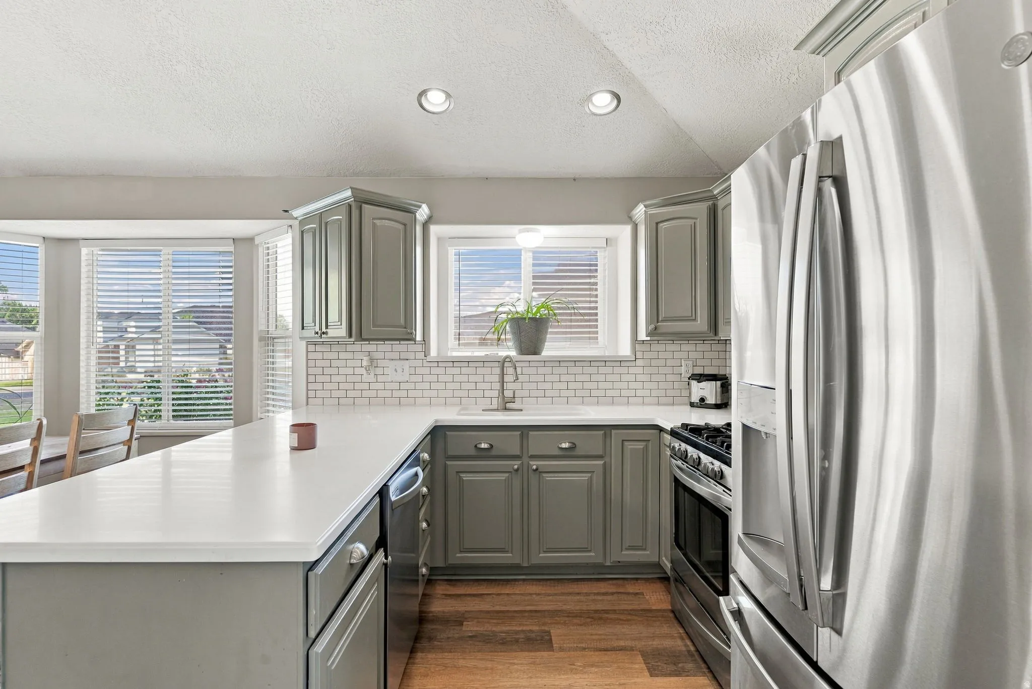 Kitchen featuring a stainless steel refrigerator, dark gray cabinetry, white subway tile backsplash, white countertops, and wood-finish flooring