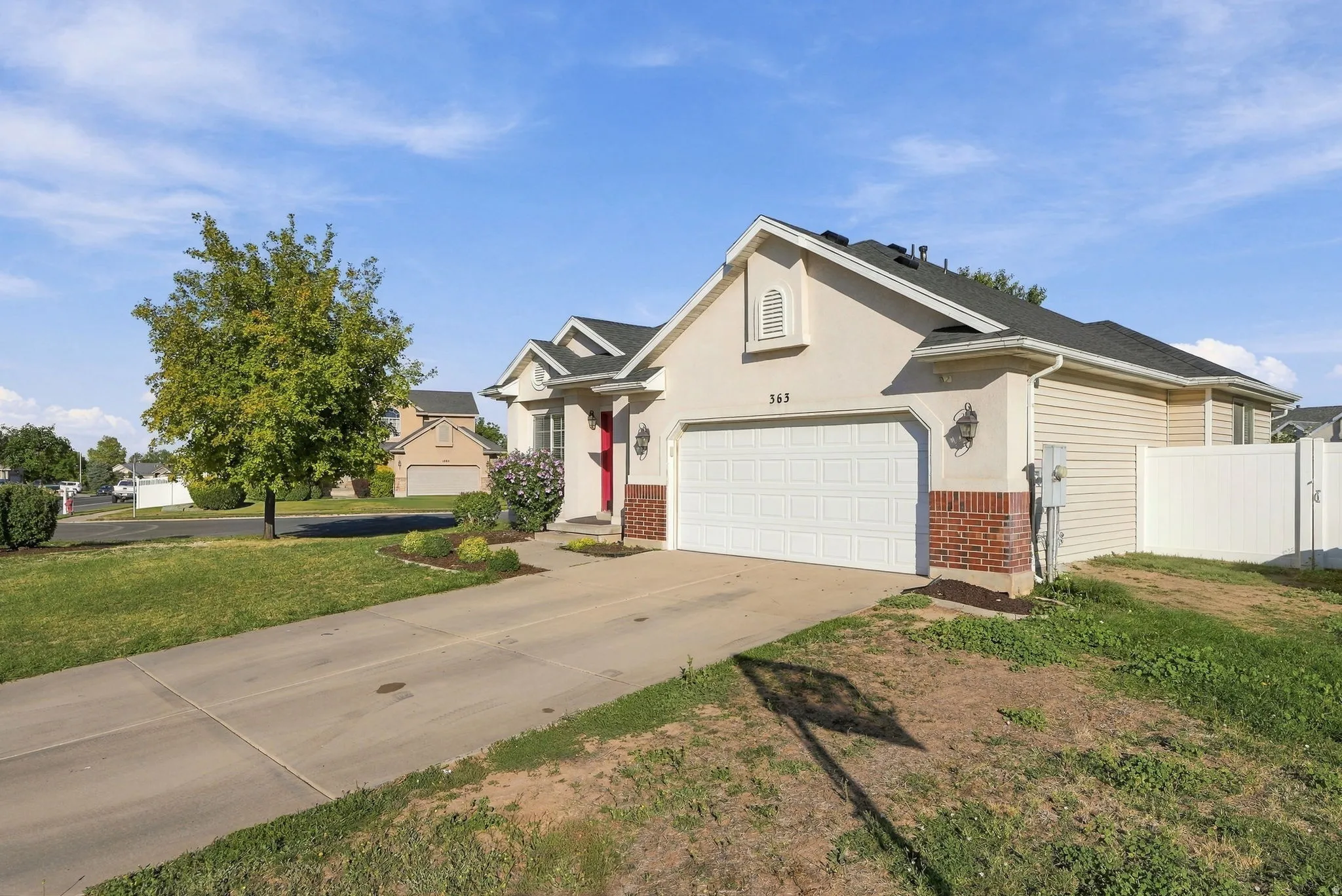 Stucco exterior with brick detailing, attached garage, concrete driveway, and white vinyl fencing