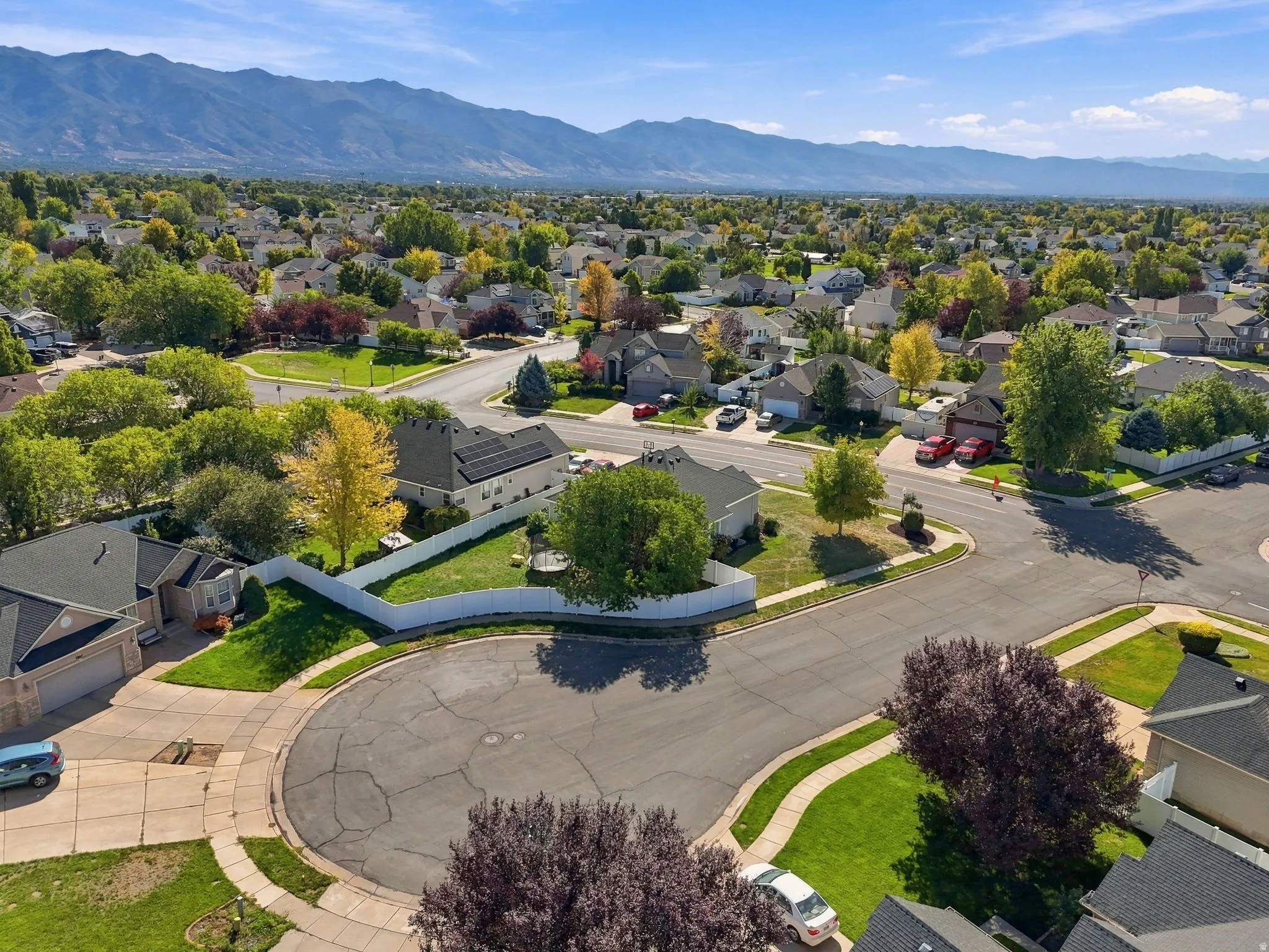 Residential neighborhood setting with extensive green landscaping, mature trees, and mountain backdrop