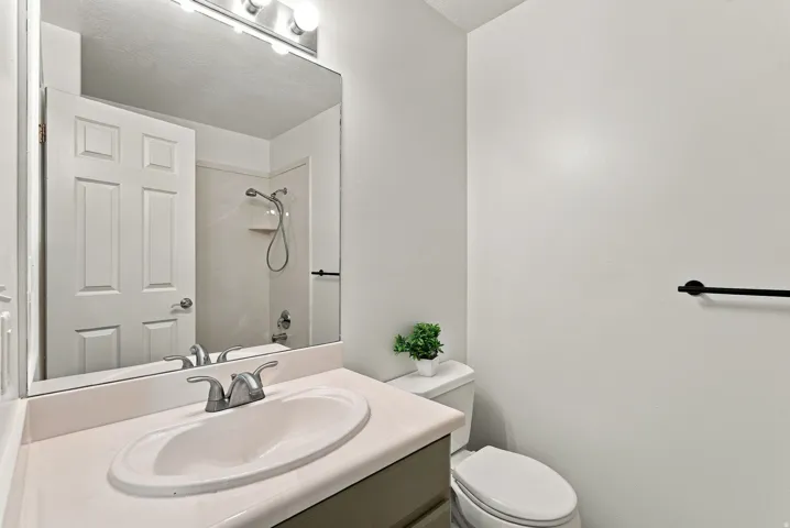 Bathroom featuring a single vanity with an integrated sink, polished chrome faucet, a wall-mounted mirror, and a toilet