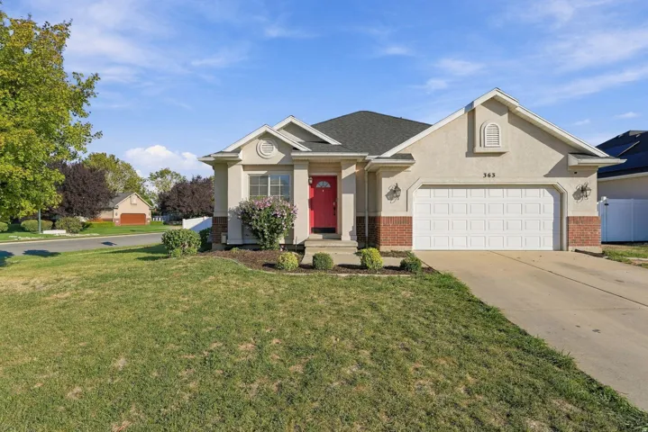 Stucco and brick exterior with a prominent garage, concrete driveway, and established landscaping