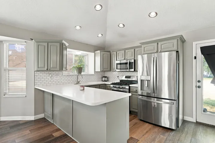 Kitchen featuring wood-finish flooring, recessed lighting, white subway tile backsplash, stainless steel appliances, and an island with a white countertop
