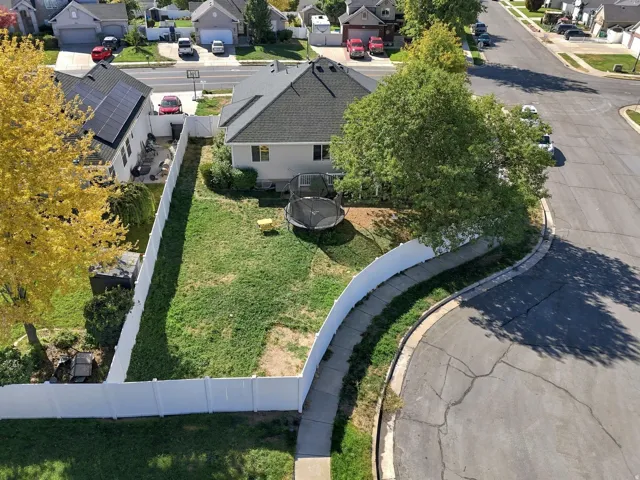 Expansive backyard with a manicured lawn, established trees, and white privacy fencing