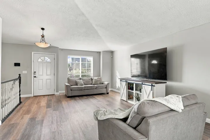 Spacious living area featuring wood-finish flooring, abundant natural light, and a white paneled entry door with an arched glass insert