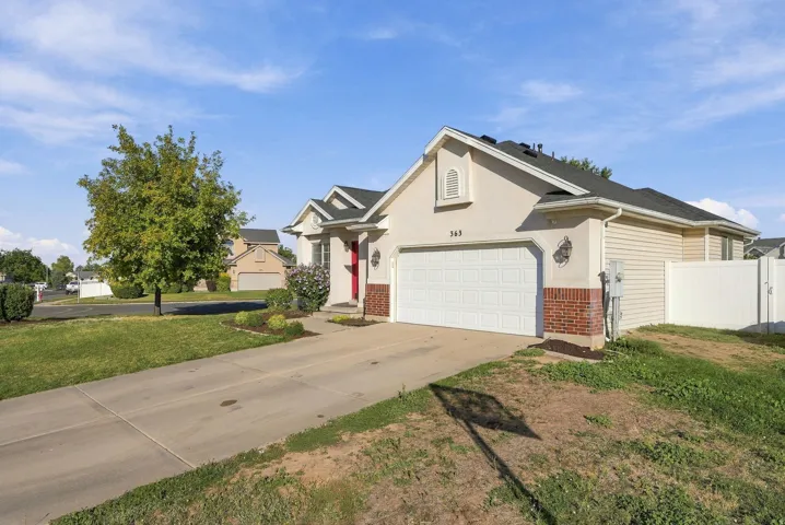 Stucco exterior with brick detailing, attached garage, concrete driveway, and white vinyl fencing