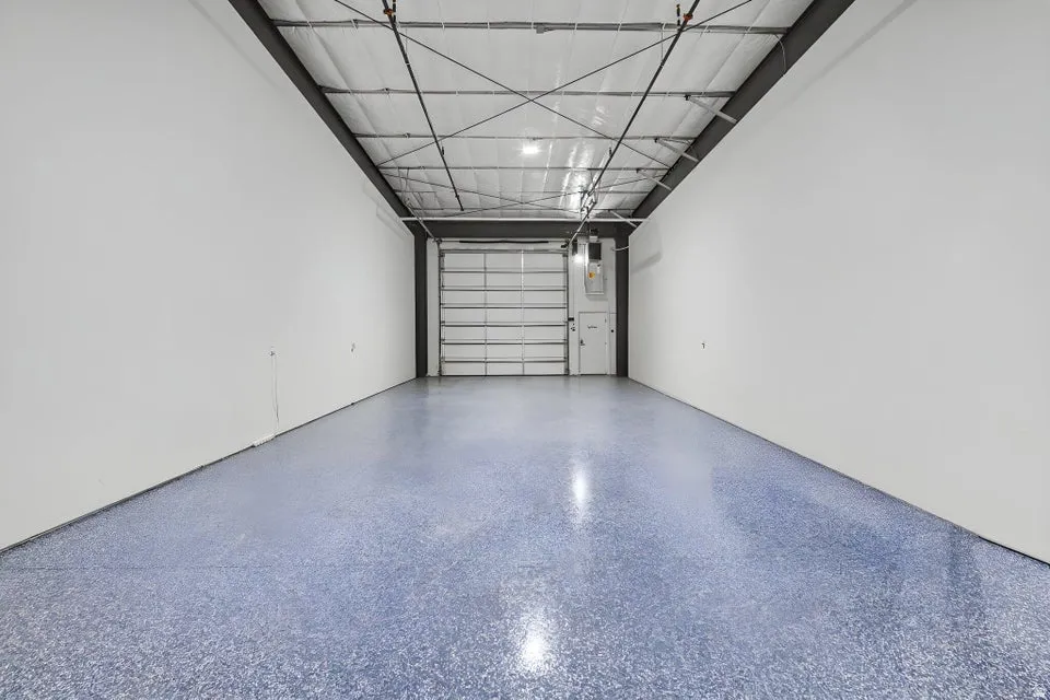 Expansive interior space featuring a roll-up garage door, a side entry door, and a high ceiling with exposed metal beams