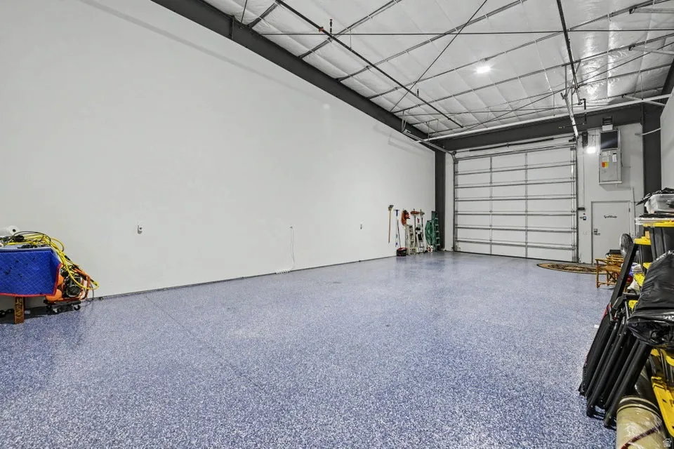 Spacious interior with an exposed ceiling, high overhead lighting, a large roll-up door, and a durable speckled floor finish