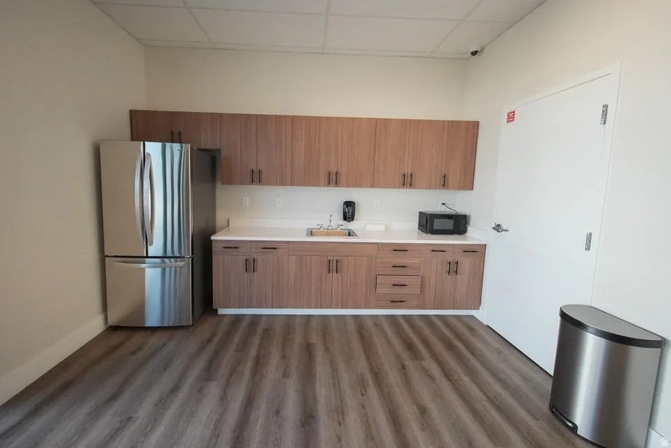 Wood-finish flooring, full-height cabinetry, stainless steel refrigerator, white countertops, and a built-in sink