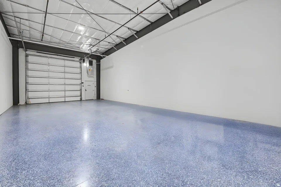 Polished concrete flooring, high ceilings with exposed structural beams, white walls, and a large roll-up door