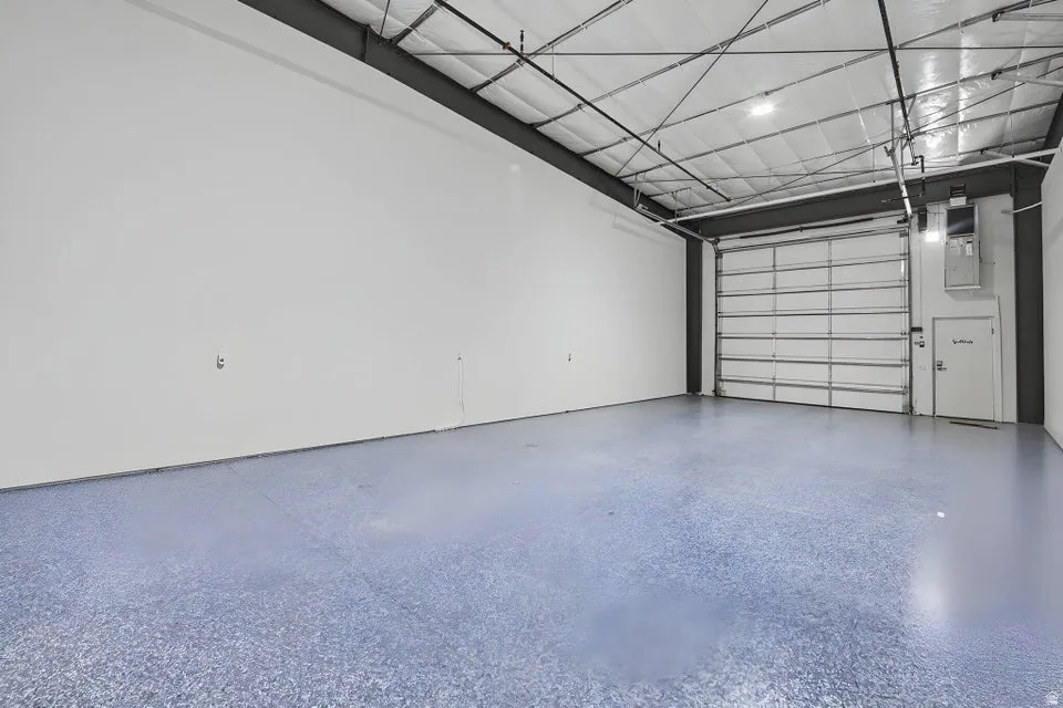 Spacious commercial interior featuring a roll-up door, high ceilings with exposed metal framing, hard surface flooring, and recessed lighting