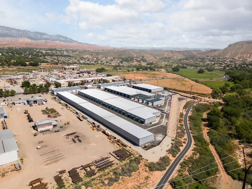 Multiple commercial buildings with metal roofs and exterior finishes, surrounded by a paved roadway and unpaved areas