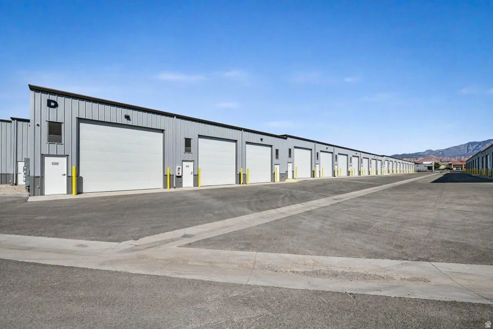 Metal-sided structures featuring multiple roll-up doors, individual pedestrian doors, exterior lighting fixtures, and a paved drive aisle