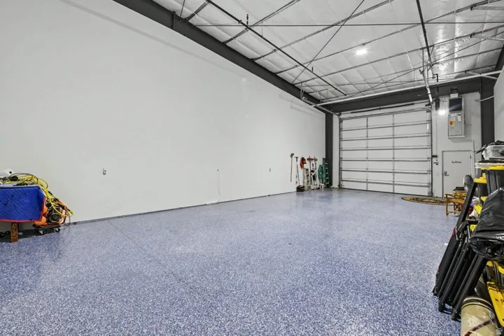 Spacious interior with an exposed ceiling, high overhead lighting, a large roll-up door, and a durable speckled floor finish