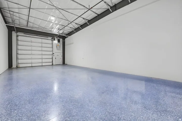 Polished concrete flooring, high ceilings with exposed structural beams, white walls, and a large roll-up door