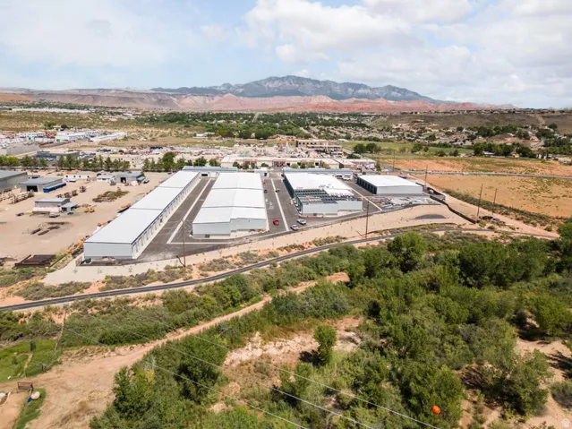 Multiple commercial buildings with white roofs and paved access, surrounded by undeveloped land and distant mountains