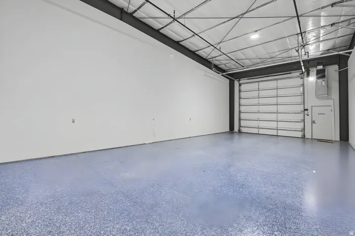 Spacious commercial interior featuring a roll-up door, high ceilings with exposed metal framing, hard surface flooring, and recessed lighting