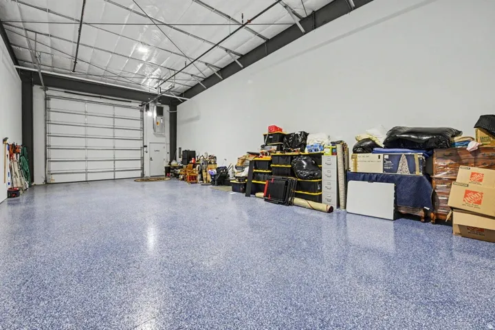 High-bay space featuring a roll-up garage door, high ceilings with exposed metal trusses, and a blue speckled epoxy floor