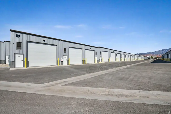 Metal-sided structures featuring multiple roll-up doors, individual pedestrian doors, exterior lighting fixtures, and a paved drive aisle
