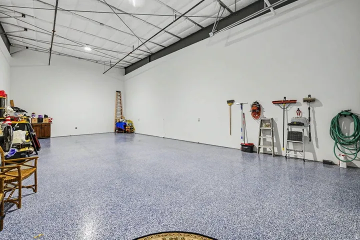 Spacious garage with high ceilings, exposed structural beams, and a speckled floor finish