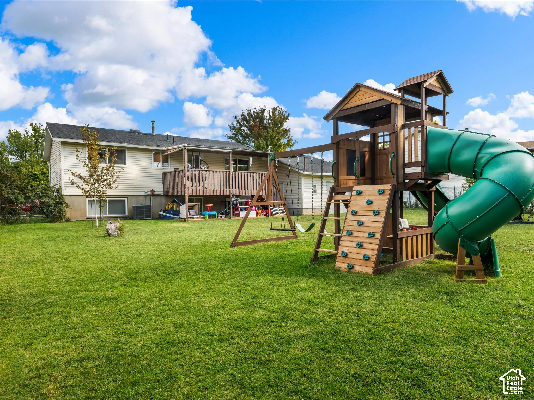 Expansive green lawn with a wood deck and an outdoor play structure featuring a slide and climbing wall