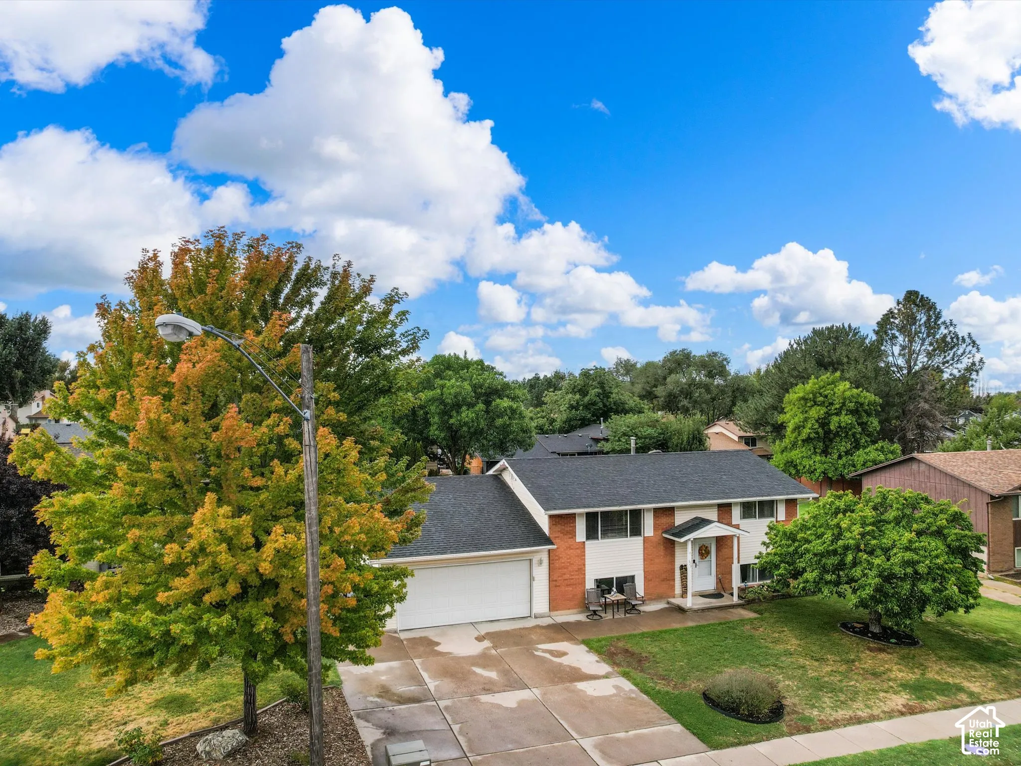 Two-story residence featuring a brick and siding exterior, an attached garage, a paved driveway, and mature landscaping