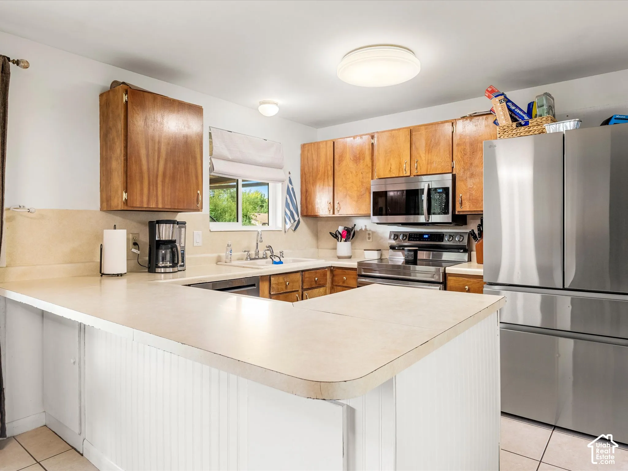 U-shaped kitchen with wood cabinetry, stainless steel appliances, and a white beadboard peninsula