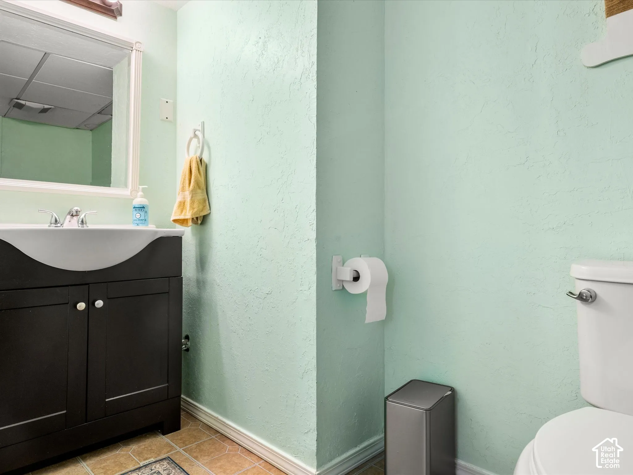 White porcelain toilet, dark wood-finish vanity with curved basin, chrome faucet, wall-mounted mirror, and tile flooring