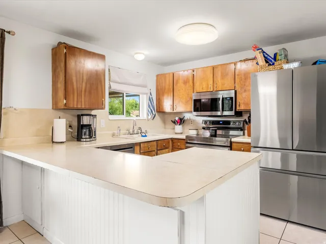 U-shaped kitchen with wood cabinetry, stainless steel appliances, and a white beadboard peninsula