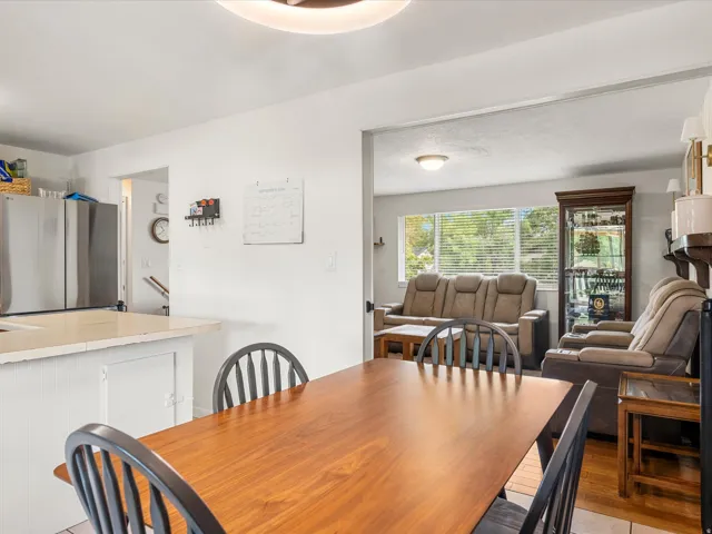 Dining area with a wood-finish table, adjacent to a living space featuring wood-finish flooring and a large window