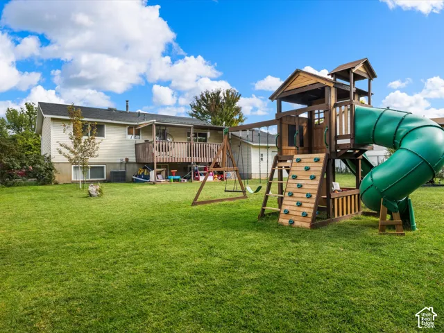 Expansive green lawn with a wood deck and an outdoor play structure featuring a slide and climbing wall