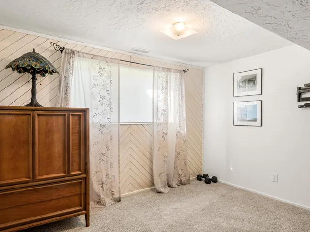 Neutral-toned carpeting paired with white walls, featuring a window with privacy blinds, and recessed lighting