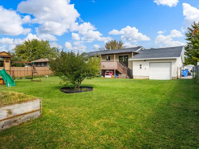 Expansive green lawn, mature tree, raised garden bed, wooden deck, attached garage with white door