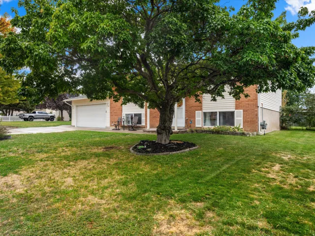 Brick exterior featuring white siding accents, an attached garage, and a lush front lawn with mature tree landscaping