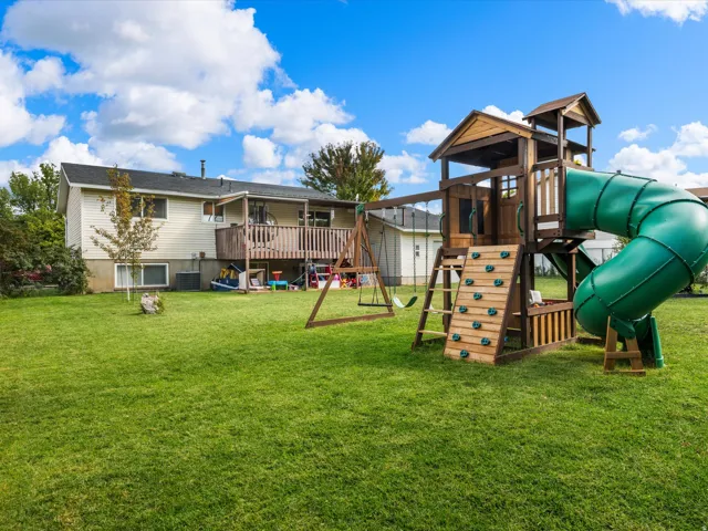 Expansive green lawn with a wood deck and an outdoor play structure featuring a slide and climbing wall