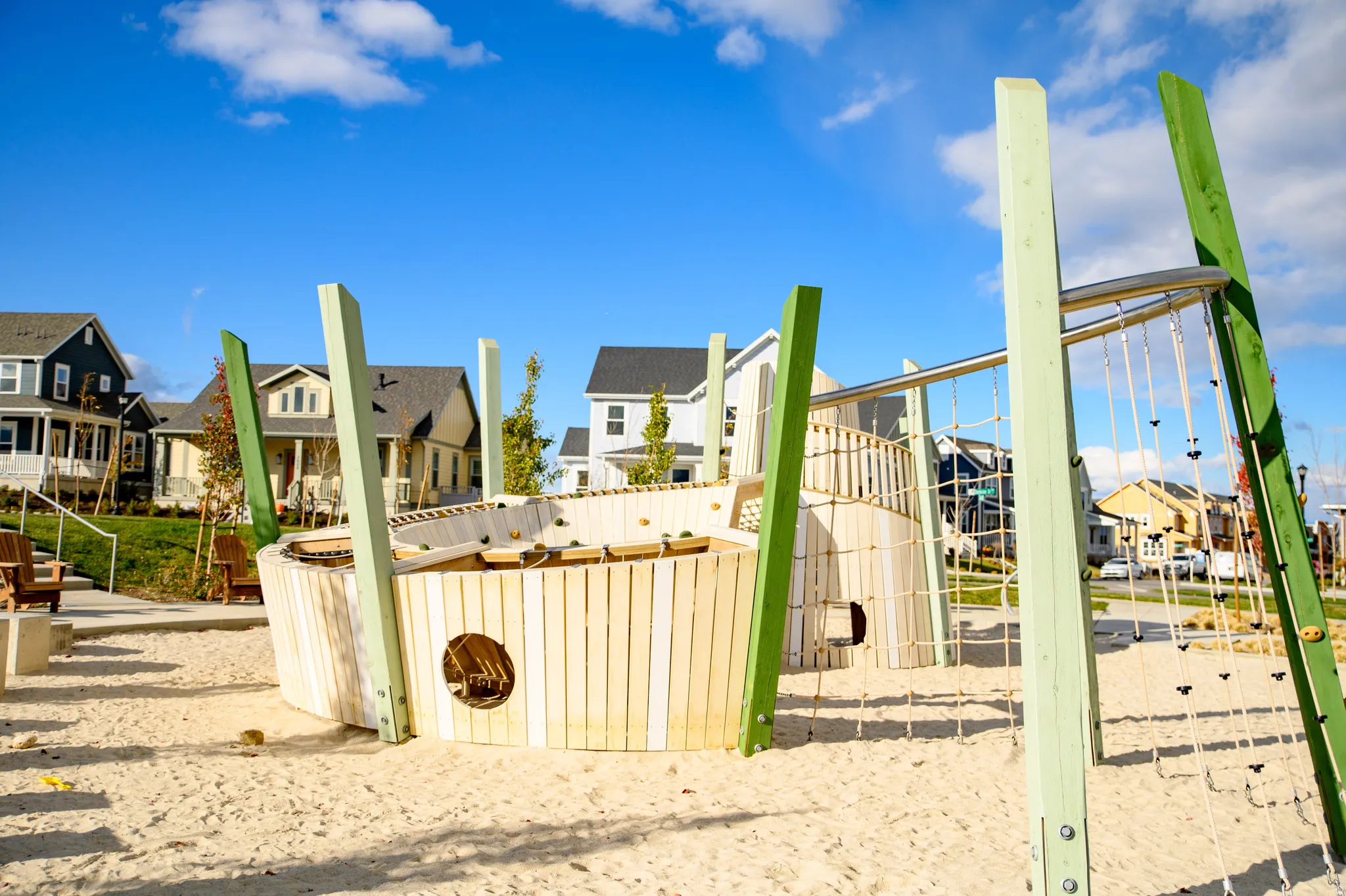 Neighborhood playground featuring a sand surface, wooden play structure, and integrated climbing ropes