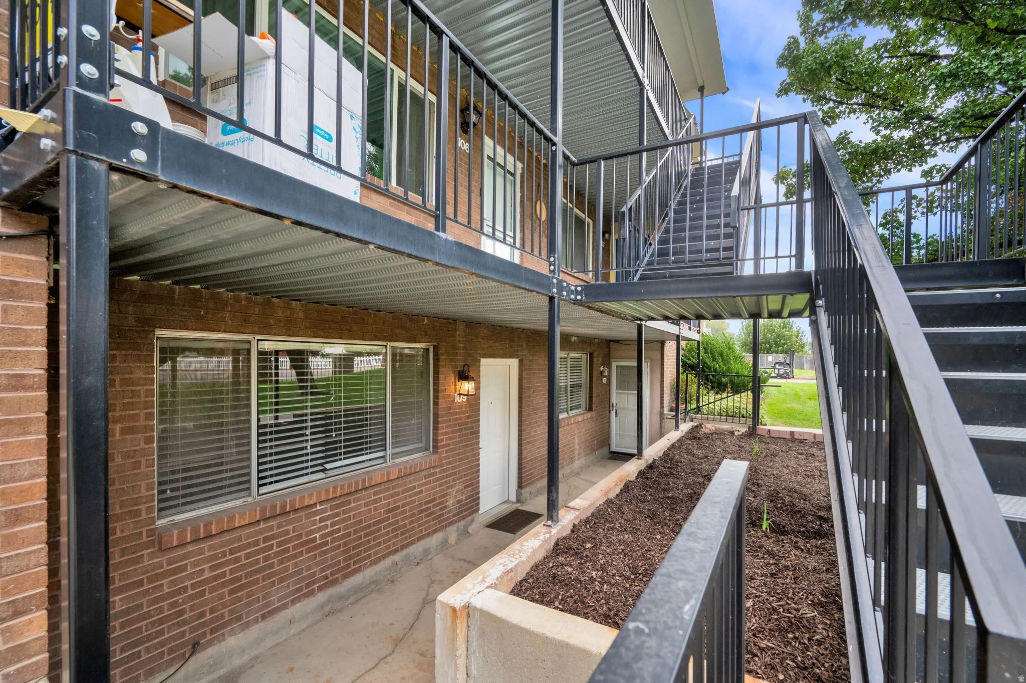Brick exterior with multiple windows, black metal railings, an exterior staircase, and a covered walkway
