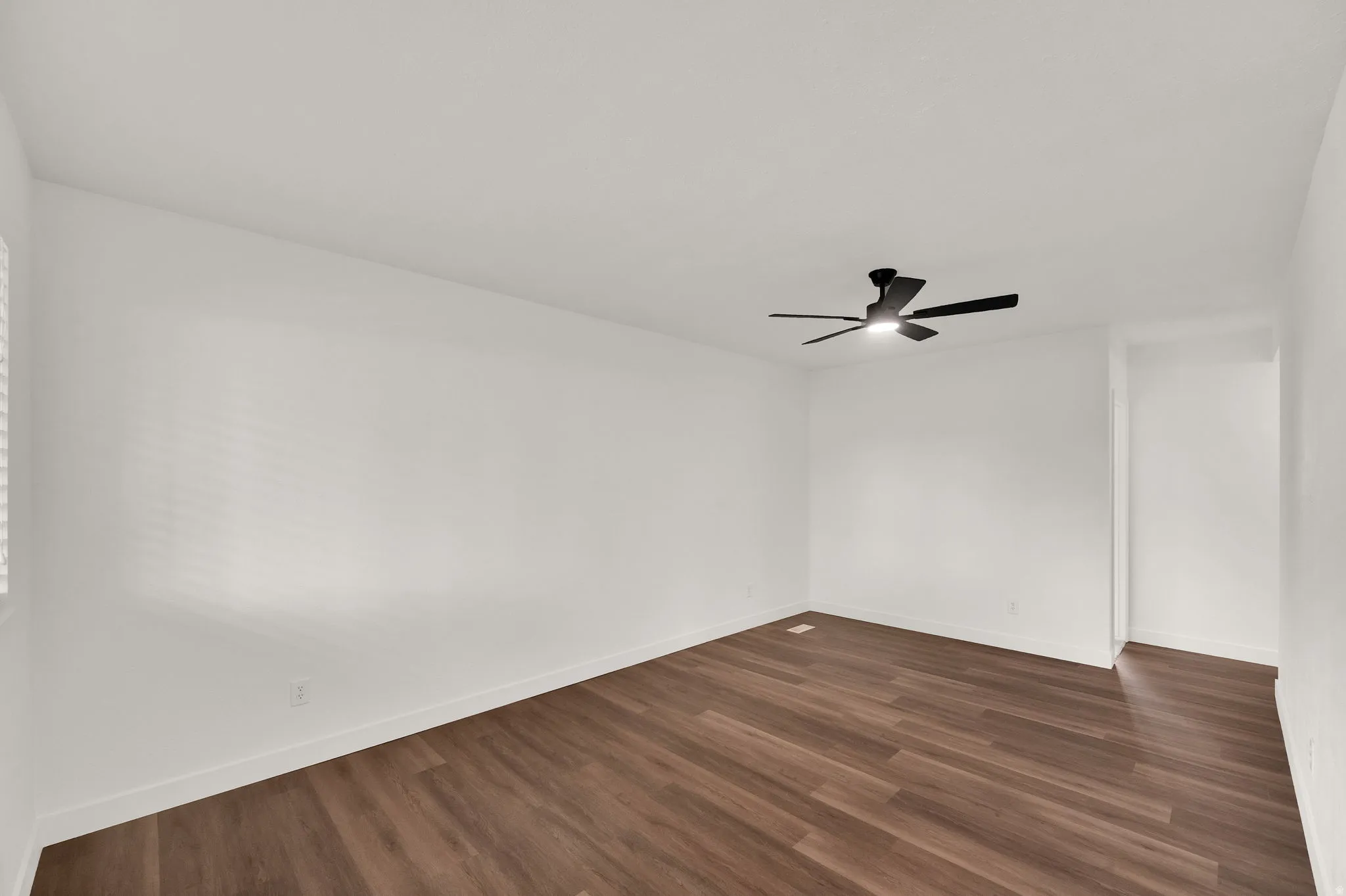 Wood-finish flooring, white walls, and a black ceiling fan with integrated lighting