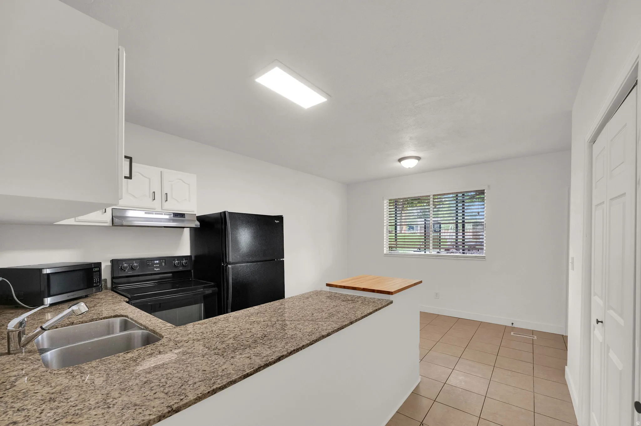 Kitchen featuring granite-finish countertops, stainless steel double basin sink, white cabinetry, integrated range hood, and tile flooring