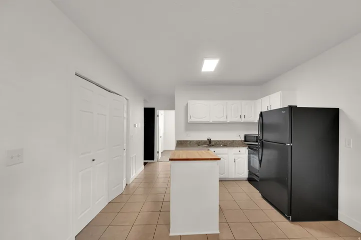 Kitchen featuring white cabinetry, a freestanding range, a black refrigerator, and tile flooring